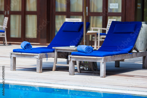 Fototapeta Blue towels on loungers near swimming pool at tropical resort