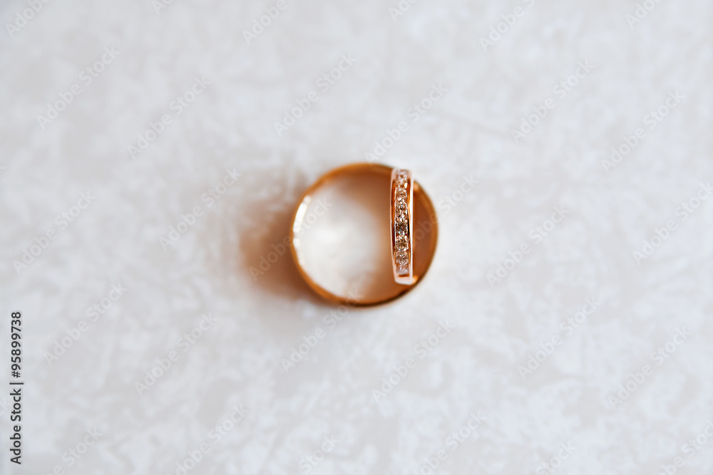Golden wedding rings with diamonds on white pattern background.