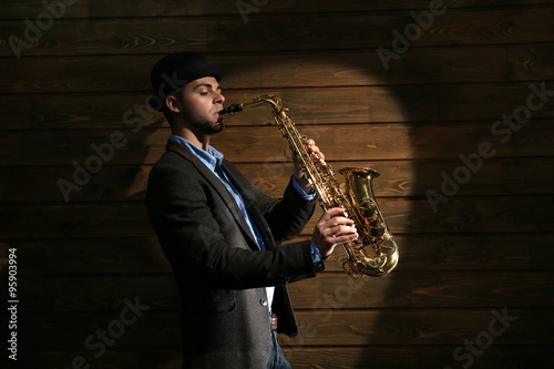 Elegant saxophonist plays jazz on wooden background