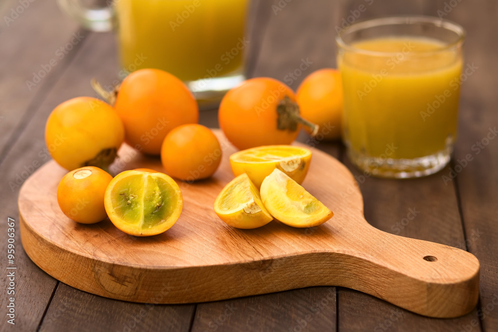 Naranjilla or Lulo fruits (lat. Solanum quitoense) on wooden board with freshly prepared naranjilla juice in the back (Selective Focus, Focus on the naranjilla pieces in the front) Naranjilla or Lulo fruits (lat. Solanum quitoense) on wooden board with freshly prepared naranjilla juice in the back (Selective Focus, Focus on the naranjilla pieces in the front)