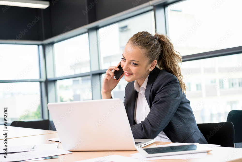 Businesswoman working & sitting at her desk in an office Businesswoman working & sitting at her desk in an office