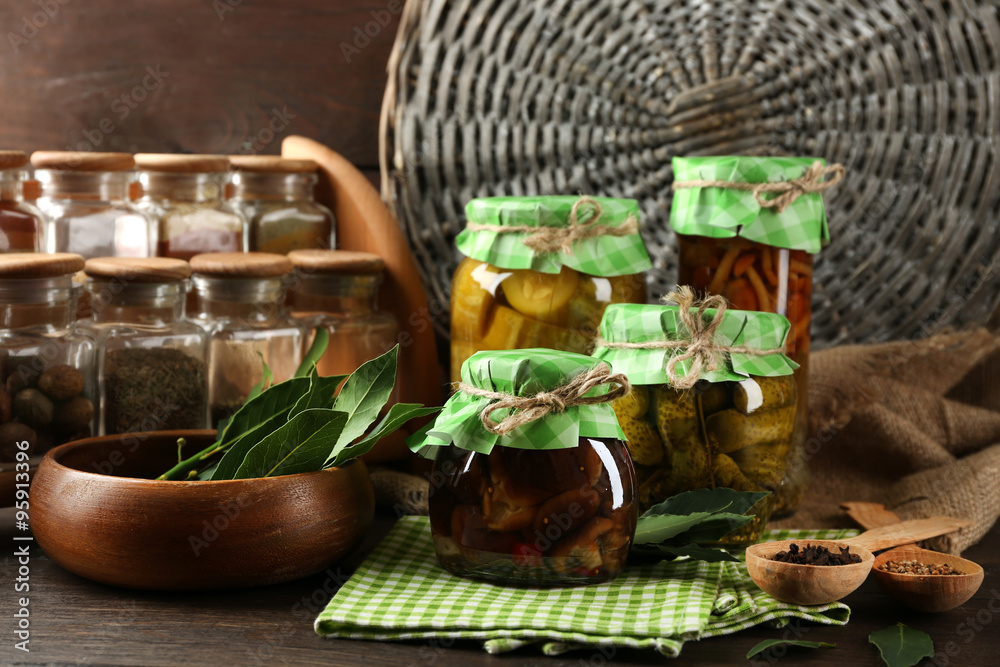 Jars with pickled vegetables, beans, spices and kitchenware on wooden background