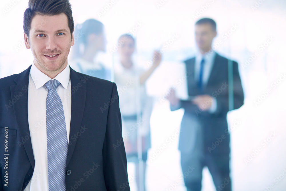 Portrait of young businessman in office with colleagues in the background Portrait of young businessman in office with colleagues in the background