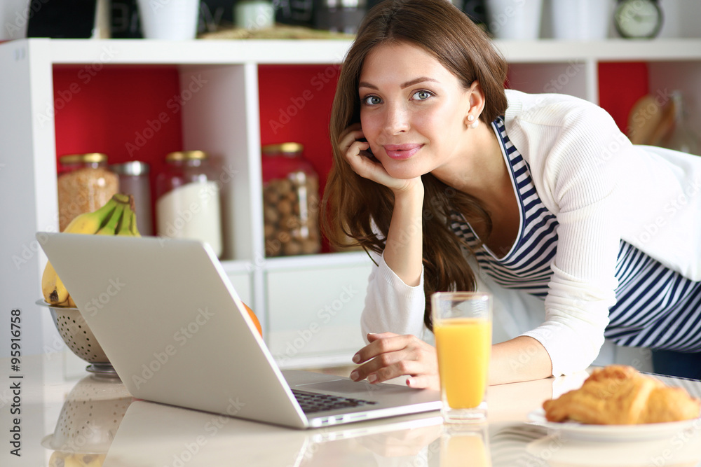 Attractive young woman using laptop and sitting in the kitchen Attractive young woman using laptop and sitting in the kitchen