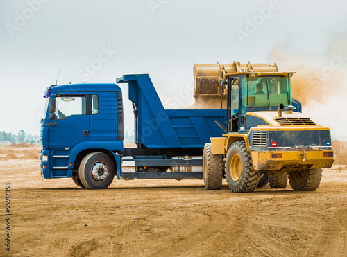 Huge backhoe loader filling the excavated soil inside blue dump truck