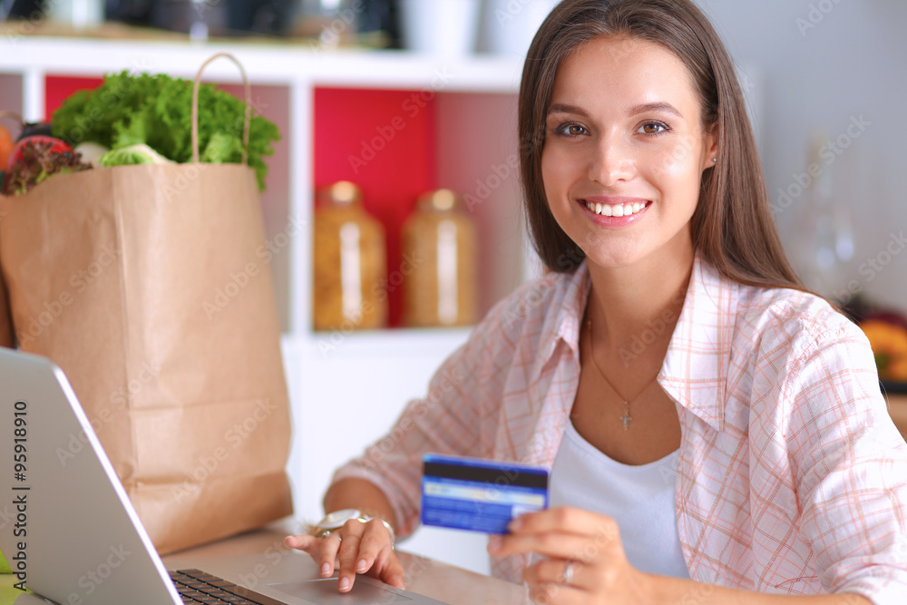 Smiling woman online shopping using tablet and credit card in kitchen Smiling woman online shopping using tablet and credit card in kitchen