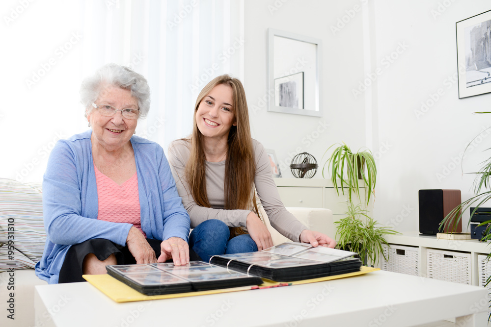 elderly woman with her young granddaughter at home looking at memory in family photo album elderly woman with her young granddaughter at home looking at memory in family photo album