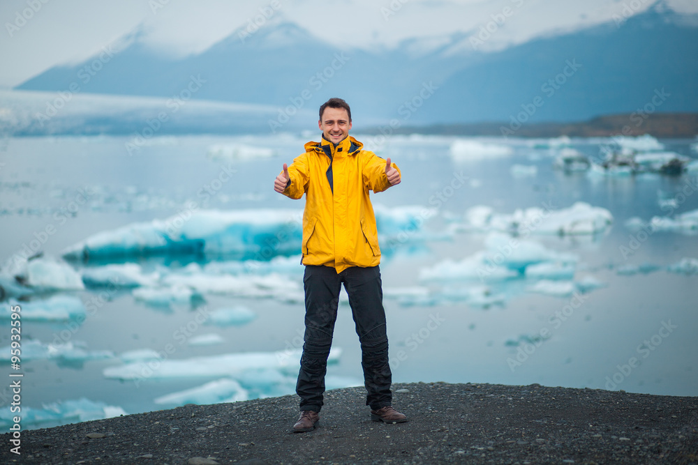 Smiling young man showing thumbs up near Jokulsarlon glacier lagoon in Iceland. Loving Iceland. Male showing thumbs up sign in winter time.