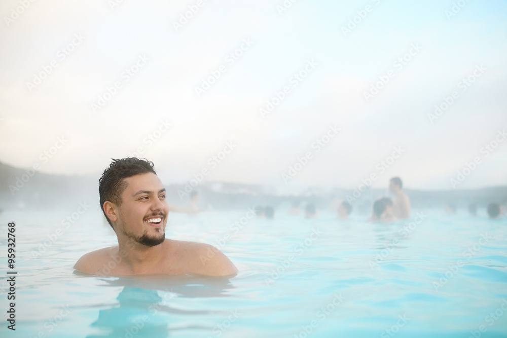 Portrait of a smiling hispanic young man relaxing in pool in Iceland.