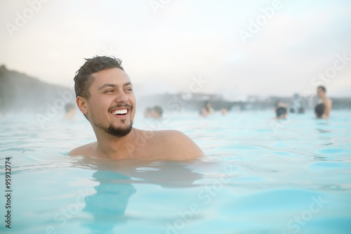 Smiling hispanic young man relaxing in pool in Iceland. Happy handsome latino male person in a blue water pool. © kegfire