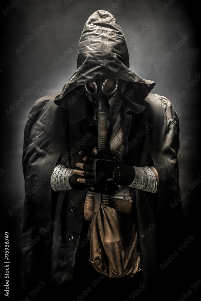 man in the gas mask in the hood, on the black background surrounded by smoke, with hands on the chest, survival soldier after apocalypse.
