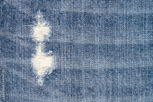 Close up texture of blue torn denim jeans with hole and threads