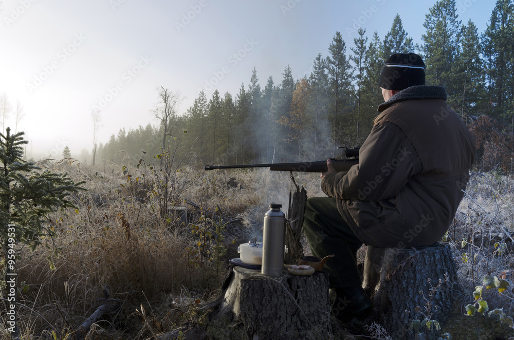Φωτογραφία Moose hunter sitting on a stump with a litle smoky fire in front holding a rifle and with a sandwich and a thermos waiting , picture from the North of Sweden