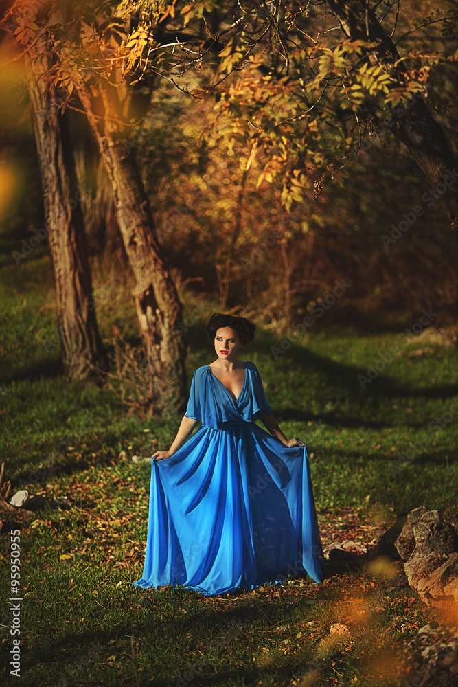Naklejka premium young women in a blue long dress at sunset in a forest .Beautiful young woman in blue dress in garden on sunset . pretty young blonde in a teal green prom dress outdoors in a field