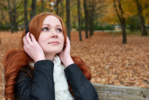redhead girl listen music in city park  fall season