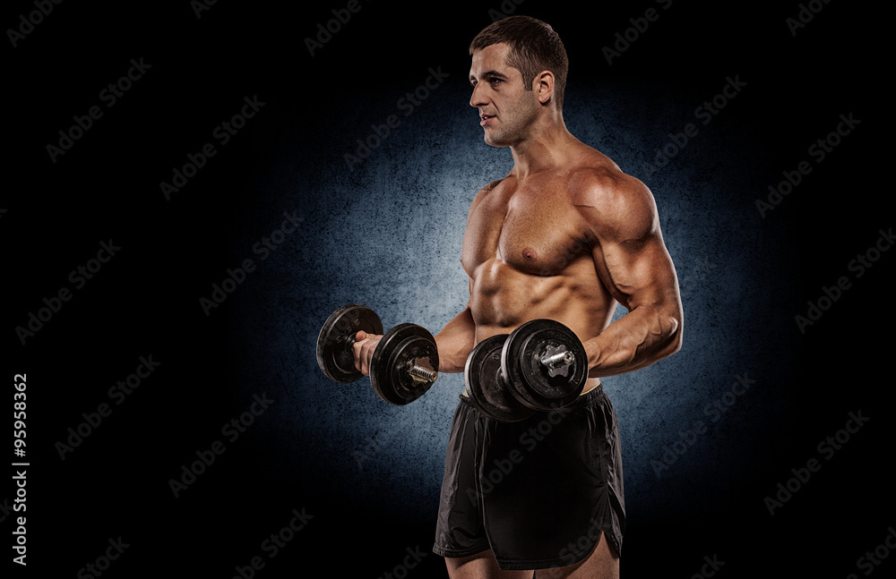 Bodybuilder doing shoulders exercises with dumbell over grey wal