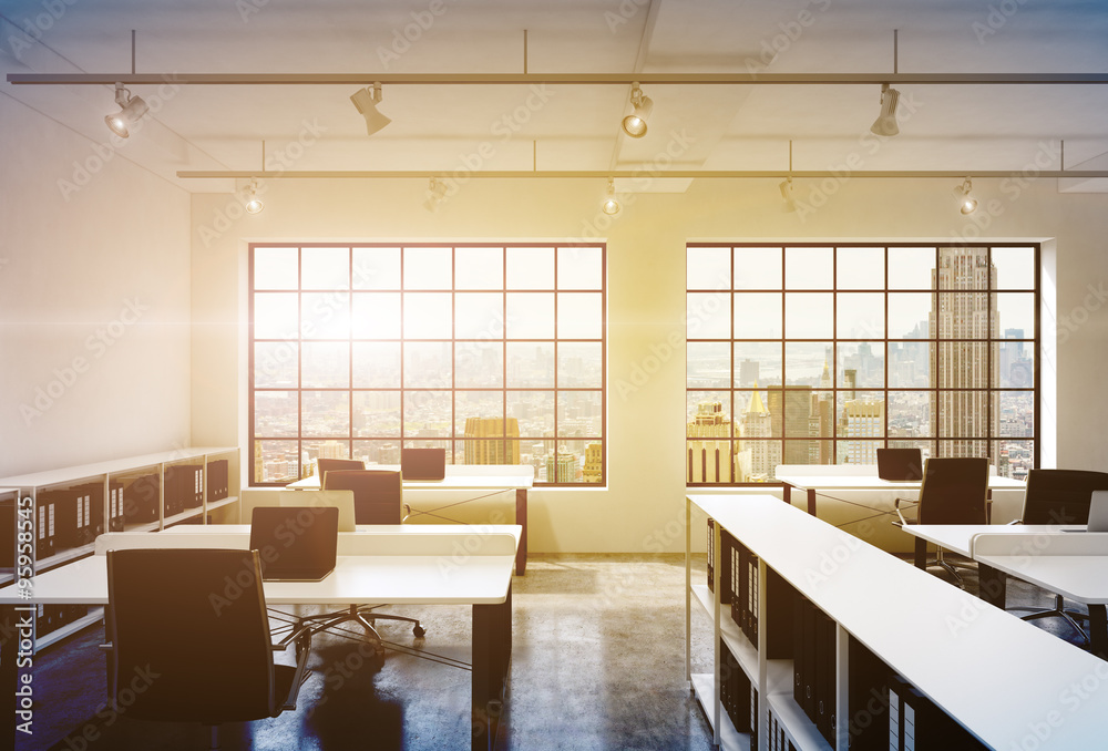 Workplaces in a bright modern loft open space office. Tables equipped with laptops; corporate documents' shelves. New York in the panoramic windows. 3D rendering. Toned image. Workplaces in a bright modern loft open space office. Tables equipped with laptops; corporate documents' shelves. New York in the panoramic windows. 3D rendering. Toned image.