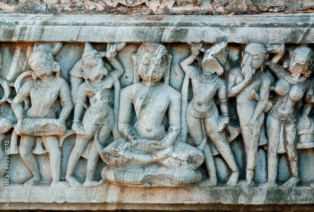 Obraz premium Buddha sitting in the crowd of people on the wall of ancient temple in India