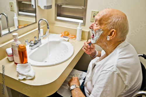 Fototapeta Naklejka Na Ścianę i Meble -  Elderly Man in Wheelchair Shaving at Bathroom Sink