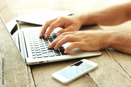 Male's hands taping on laptop on wooden table in office