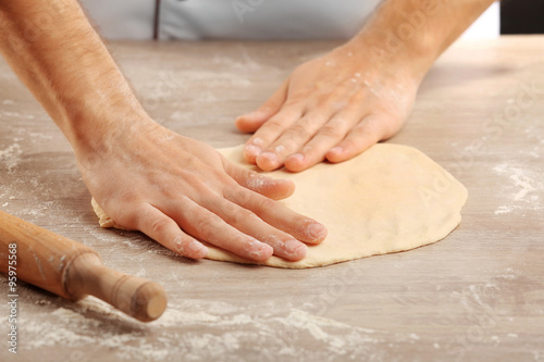 Hands preparing dough basis for pizza on the wooden table, close-up © Africa Studio