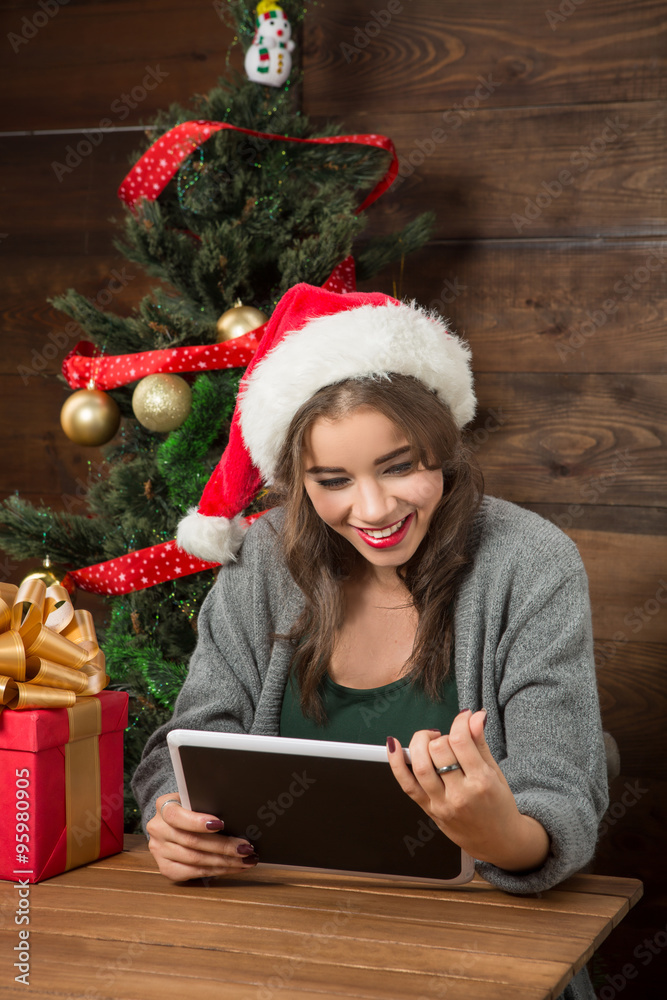 Beautiful girl sitting at the table with a tablet PC near New Year tree Beautiful girl sitting at the table with a tablet PC near New Year tree