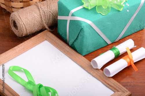 Blank photo frame with christmas gift box, white paper with bow on wooden table.