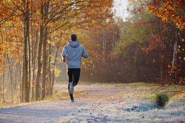 Young man running at park during autumn morning.