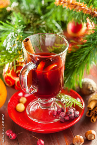 Glass of mulled wine by Christmas tree with decorations. Delicious drink for party.