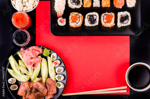 Sushi set, soy sauce, ginger, wasabi, black and red roe, avocado, salmon, cheese on black and red background. Free space for your text