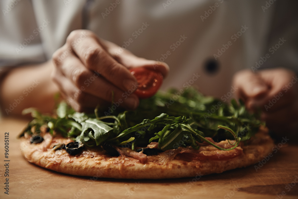 Italian chef cooking pizza on wood table in the kitchen. Close-up of fresh delicious pizza with greens and tomatoes. 