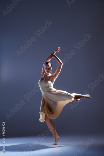 Fototapeta Naklejka Na Ścianę i Meble -  Young beautiful dancer in beige dress dancing on gray background