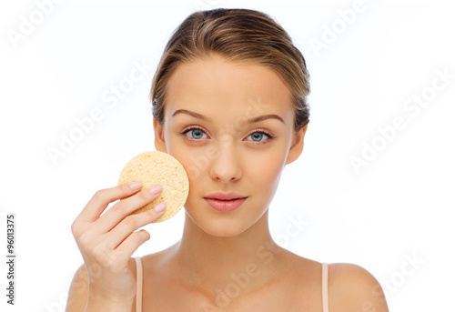 young woman cleaning face with exfoliating sponge