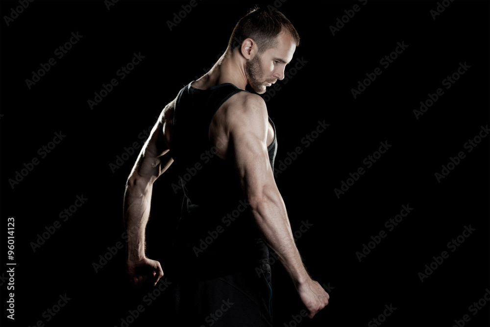 muscular man, clasps hands in fist, black background, place for text on the right muscular man, clasps hands in fist, black background, place for text on the right