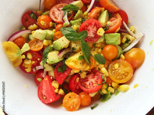 Overhead view of summer salad with cherry tomatoes, avocado, fresh corn, red onion and basil