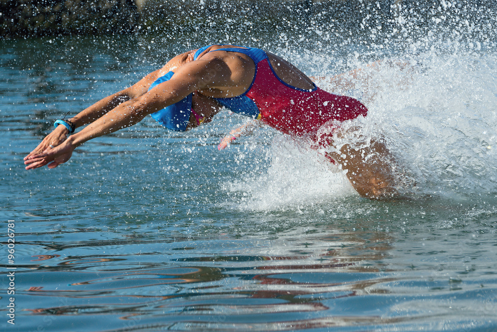 Triathlon participants running into the water for swim portion of race. Splash of water and athletes running. Focus on water splash.