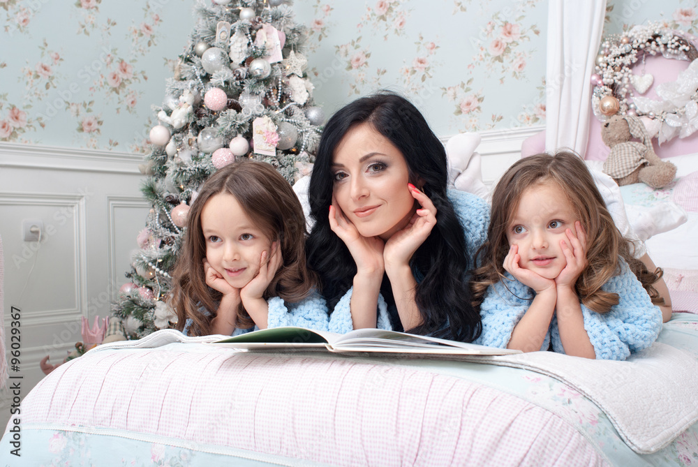Молодая женщина с дочерьми на кровате читают сказки и мечтают - obrazy, fototapety, plakaty 