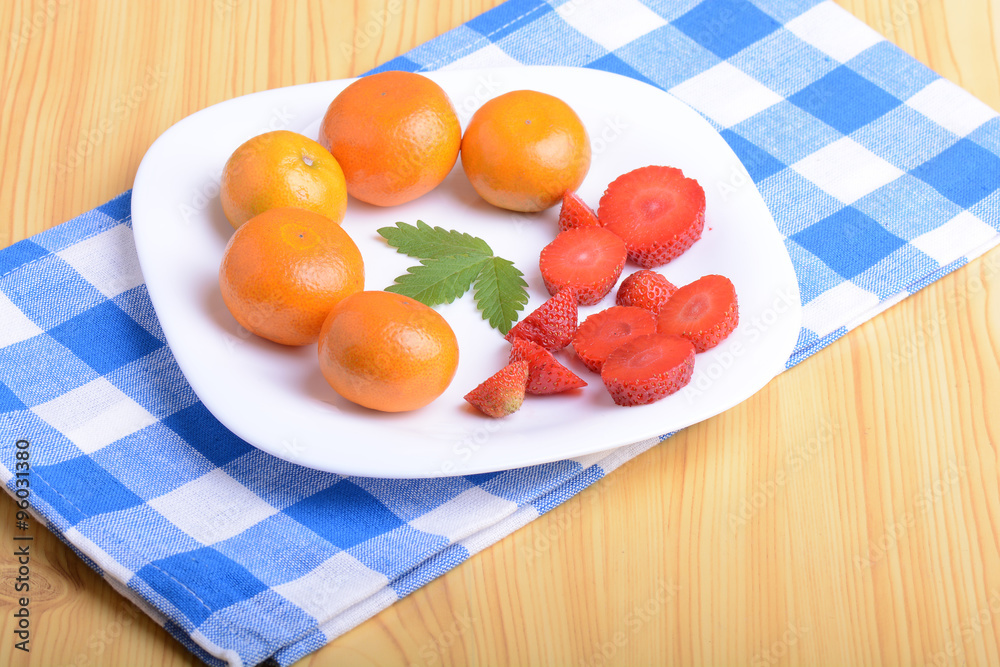 A slice of red strawberry on white plate with mandarin and strawberry slices A slice of red strawberry on white plate with mandarin and strawberry slices