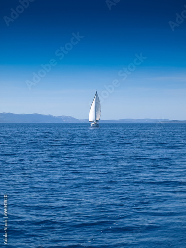 Front view of a sailing boat in an open blue sea and a clear blue sky
