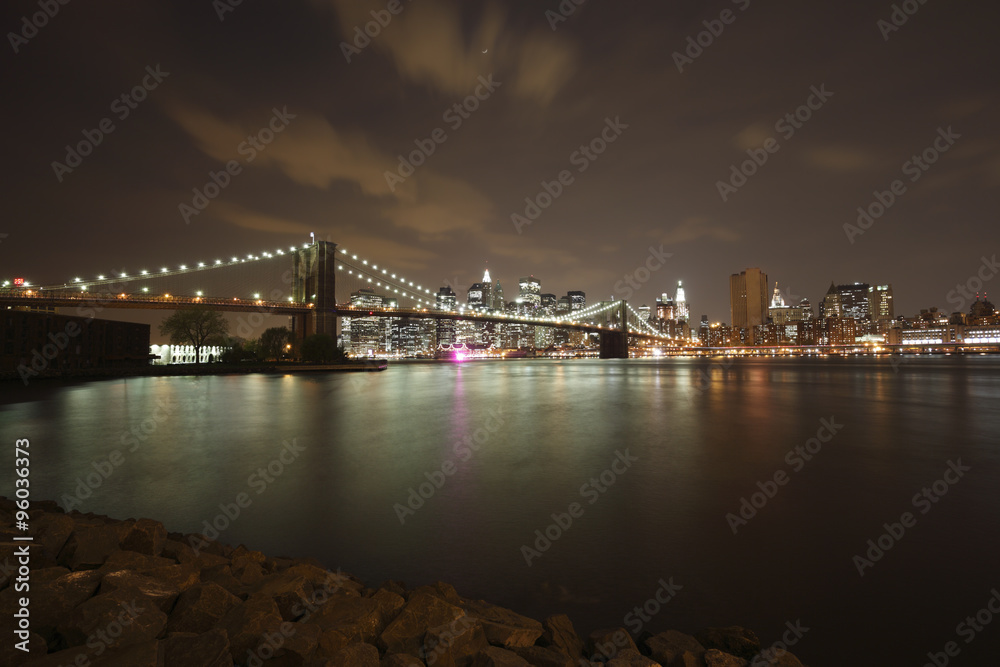 Wide angle view of the Brooklyn Bridge and Manhattan skyline as seen from across the East River at dusk.