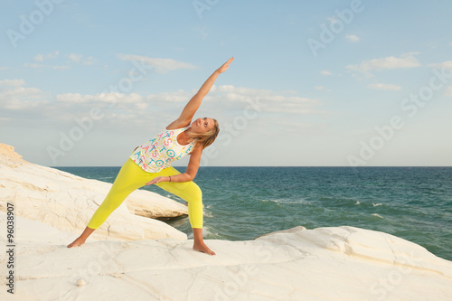 Young women doing yoga by the sea - Bikram triangle pose (Trikonasana Bikram)