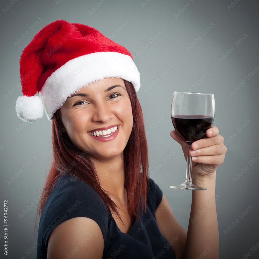 A beautiful young woman wearing Santa hat and holding glass of red wine A beautiful young woman wearing Santa hat and holding glass of red wine
