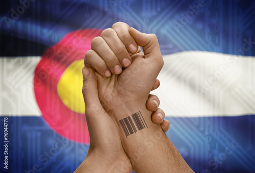 Barcode ID number on wrist of dark skinned person and USA states flags on background - Colorado photo