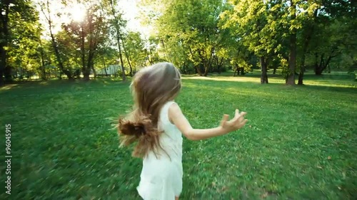 Girl running away from camera in the park. Happy schoolgirl in the white dress. Lens flare