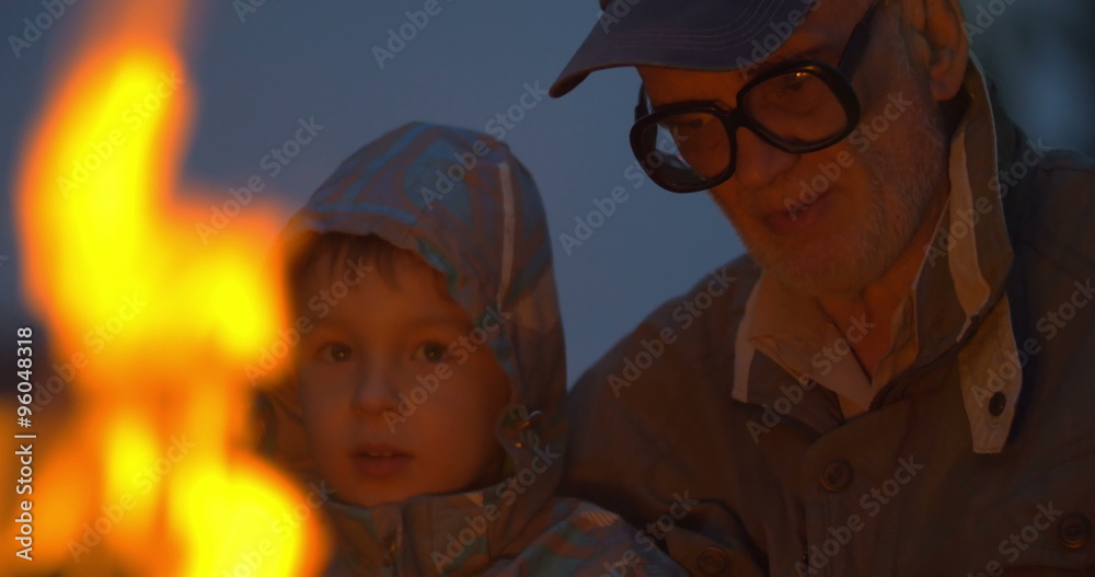 Elderly man sitting with small boy near campfire Elderly man sitting with small boy near campfire
