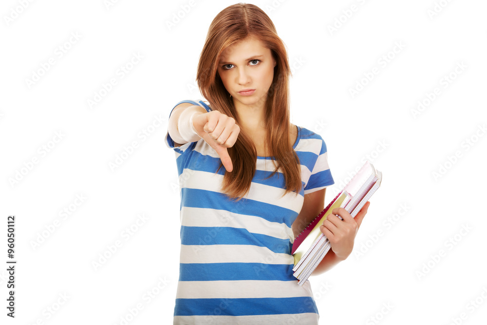 Teenage woman holding a books and shows thumb down Teenage woman holding a books and shows thumb down