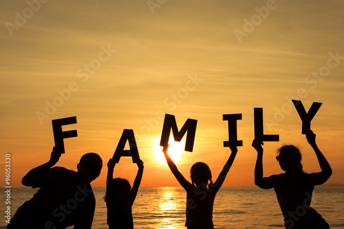 Happy family standing on the beach at the sunset time.