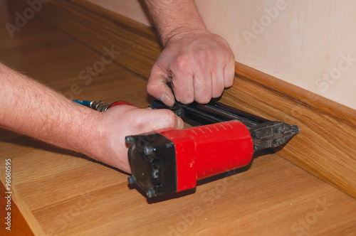 Assembly of wall clips for skirting board. Repairman's hands Installing Skirting Board Oak Wooden Floor. Screwing Chipboard