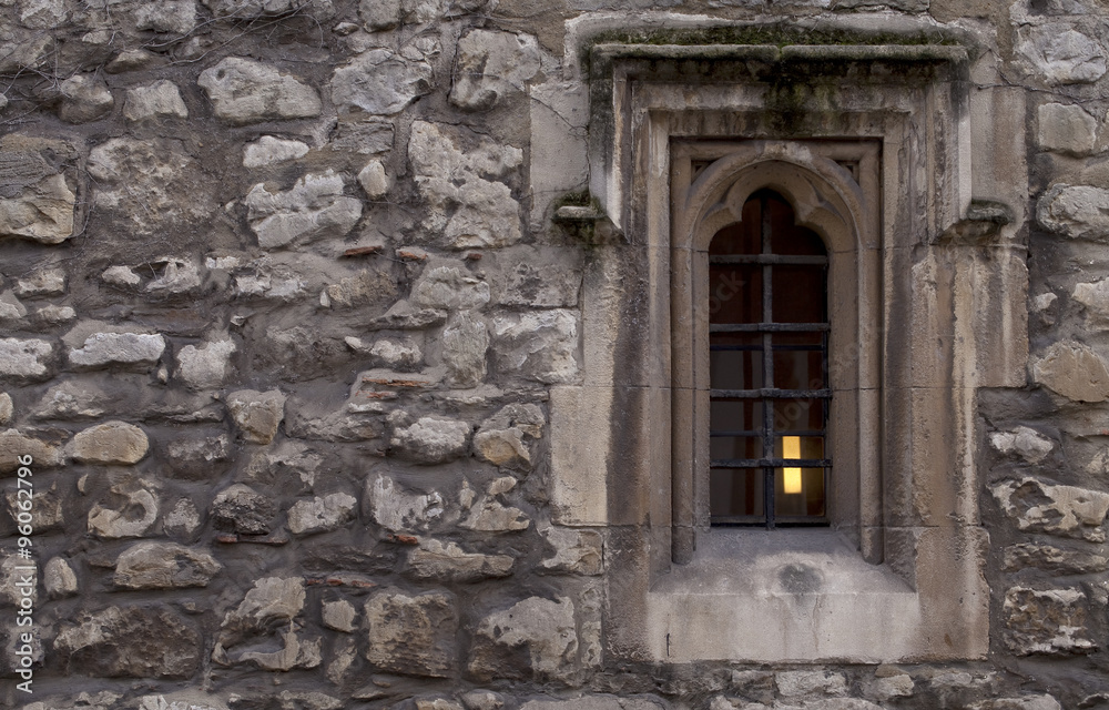 Monk's Window. A small window in an old wall of an abbey.  A lamp burns inside behind the black wrought iron bars.