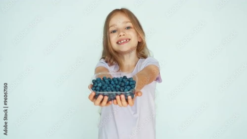 Girl sniffing blueberry and showing at camera on the white background. Happy child with fruits Girl sniffing blueberry and showing at camera on the white background. Happy child with fruits